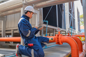 Young engineer working at large factory,Technician in protective uniform and with hardhat  checking temperature in pipes
