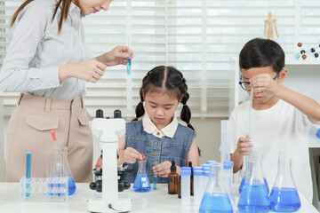 Two asian school children conducting science experiment using pipette and beaker under supervision...