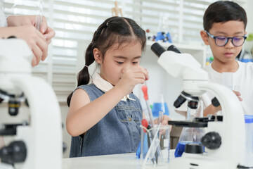 Asian girl in denim outfit learning chemistry mixing liquids with pipette next to microscope while...