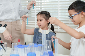 Asian girl and boy holding test tubes with blue liquid examining chemical reaction while standing next to caucasian teacher in science class using laboratory equipment during chemistry activity
