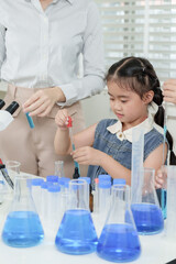 Asian girl in elementary class using pipette during science lesson with assistance from female...