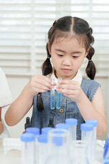 Asian elementary girl student mixing chemicals with test tubes during hands-on science experiment...