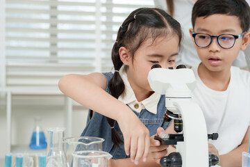 Asian girl looking into microscope with guidance from classmate during elementary science class...