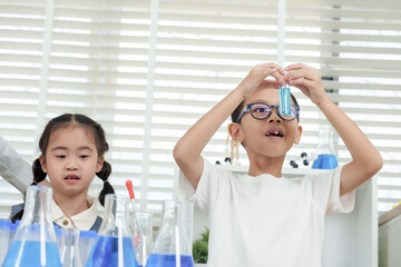Asian elementary boy lifting test tube with curiosity and excitement during science class...