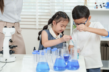 Asian elementary children using pipettes together during school science class pouring blue chemical...