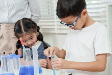 Asian girl smiling while watching boy pour blue liquid into test tube during elementary school...