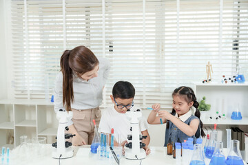 Asian elementary students working with microscope and test tubes during science experiment assisted...