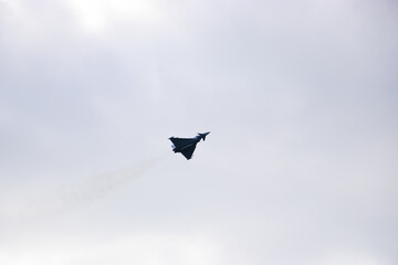 Military fighter jet in flight against a clear pale blue sky. Dark silhouette of aircraft with...