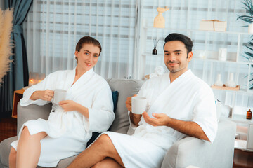 Fototapeta premium Beauty or body treatment spa salon vacation lifestyle concept with couple wearing bathrobe relaxing with drinks in luxurious hotel spa or resort room. Vacation and leisure relaxation. Quiescent