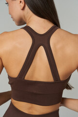 Woman in brown sports bra viewed from behind, showcasing defined musculature and stylish racerback...