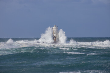 Fierce waves crashing against old lighthouse amid rough sea and strong winds