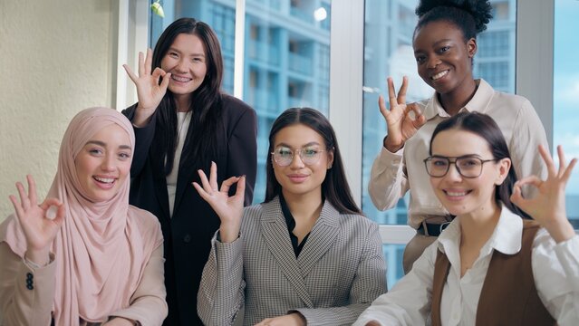 Smiling happy portrait African American Korean Indian Arabian Muslim multiethnic women females girls businesswomen looking at camera showing ok sign gesture good approval okay reaction inside office - Powered by Adobe