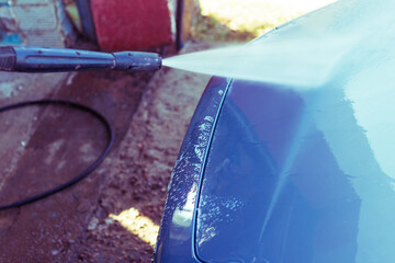 Car washing with high-pressure water spray at an outdoor facility on a sunny day