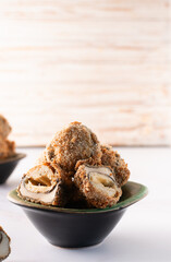 Crispy mushroom balls with cheese and spices baked in bread crumbs in dark ceramic bowl on on light kitchen table close up. Healthy homemade snack.