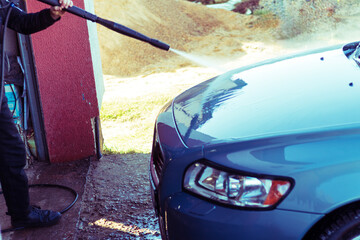 Car washing with high-pressure water spray at an outdoor facility on a sunny day