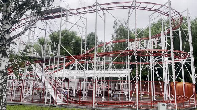 A bright and colorful children's amusement park featuring an empty roller coaster, carousel, and other fun rides. The scene is captured during a cloudy day, with no people.