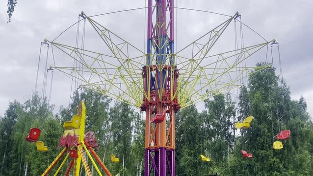 A bright and colorful children's amusement park featuring an empty roller coaster, carousel, and other fun rides. The scene is captured during a cloudy day, with no people.