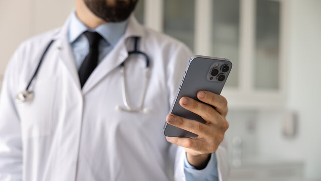 Close up banner shot of smartphone in hand of male doctor. Medical practitioner, healthcare professional man chatting with patient on cellphone, giving online support, remote consultation - Powered by Adobe