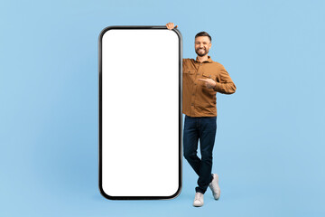 Smiling man pointing at big blank smartphone screen. Large mobile mockup ideal for digital ads, app...