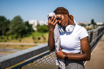 Portrait of exhausted African-American woman looking disappointed and worried while wiping sweat...