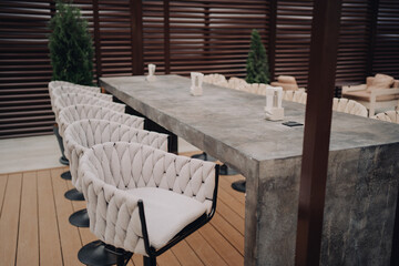 Outdoor minimalist setting featuring a long concrete table surrounded by modern upholstered chairs, ideal for gatherings, meetings, or casual dining, combining contemporary design with warm social amb