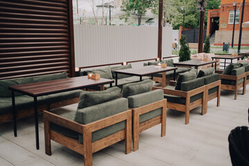An outdoor seating area featuring wooden chairs with green cushions and matching tables. Ideal for cafes, restaurants, or casual dining settings in a cozy outdoor environment.