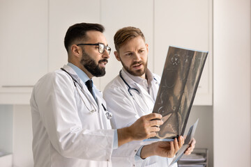 Two neurology doctors looking at X-ray, holding scan shots against light, discussing tomography results, diagnosis, trauma, tumor, collaborating on patient case, working together