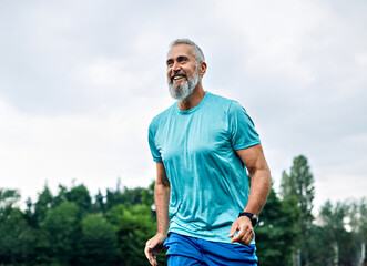 Smiling active mature middle aged man jogging running in the park