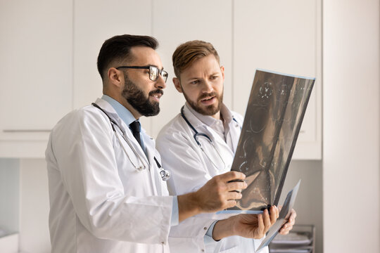 Two neurology doctors looking at X-ray, holding scan shots against light, discussing tomography results, diagnosis, trauma, tumor, collaborating on patient case, working together