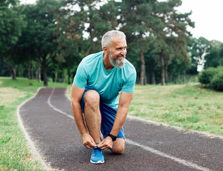 Portrait of a mid age mature sport man smiling happy and confident, prepering for exercise, tying shoe laces. Running in city park outdoors