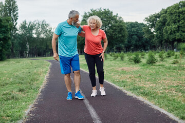 Active mid age mature couple jogging together, helping and supporting each other with a injury...