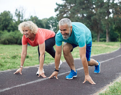 Smiling active mid aged couple standing in start position, jogging running and walking doing fitness in the park