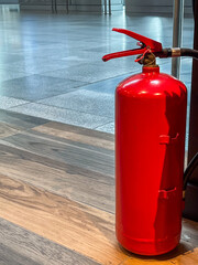 Red fire extinguisher positioned near wooden flooring in a modern building, showcasing safety...
