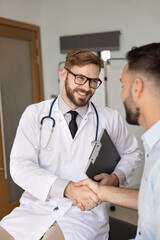 Happy handsome practitioner man in glasses and white coat giving handshake to healthy patient,...