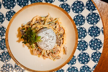 Boiled egg with spices, light salad of meat, cheese and vegetables with herbs, in a deep painted plate in the restaurant