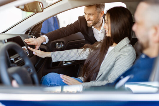 Car dealer explains vehicle features to couple sitting inside new car. Hands on experience and consultation with friendly guidance in a modern dealership, closeup shot