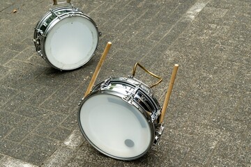 Two snare drums and drumsticks lying on cobblestone street