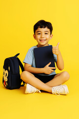  Happy Schoolboy Sitting with Notebook and Backpack on Yellow Background