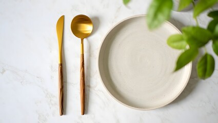 Minimalist flat lay of plate with gold cutlery and green leaves for food photography and design
