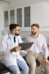 Serious Latin general practitioner man asking male patient about health complaints, listening,...