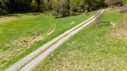 A winding gravel path through lush green fields surrounded by trees, capturing the essence of spring. Ideal for nature enthusiasts and outdoor activities.