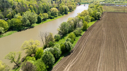 Aerial view of a serene river winding through lush green trees and a freshly plowed field under a...