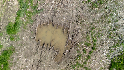 Aerial view of muddy ground with visible tire tracks and a small puddle. The scene showcases earth...