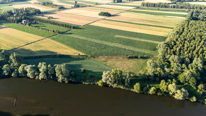 Aerial view of green and golden fields bordered by trees and a calm river, illustrating the beauty...