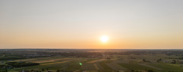 Sunset over a vast landscape, showcasing rolling fields and a serene sky. The warm hues create a...