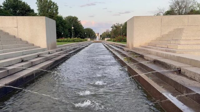 Tranquil water feature flows between symmetrical stone steps, surrounded by lush greenery and vibrant flower beds, creating a serene atmosphere in an urban park, inviting relaxation and reflection