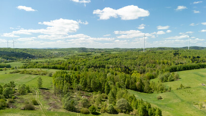 Aerial view of lush green hills and fields under a bright blue sky with scattered clouds and wind...