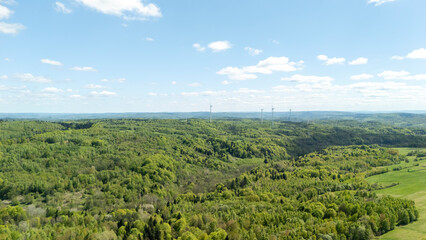 Aerial view of lush green hills under a bright blue sky with fluffy clouds. This serene landscape...