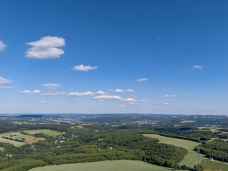 Aerial view of lush green hills under a clear blue sky with scattered clouds. This serene landscape...