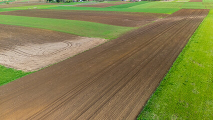 Aerial view of freshly plowed farmland featuring rich brown soil and vibrant green patches,...